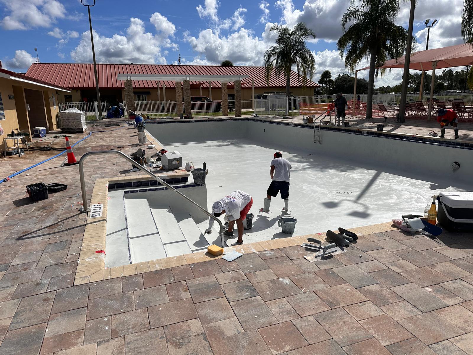 Workers resurfacing an empty swimming pool with new tile, restoring the surface after years of wear.